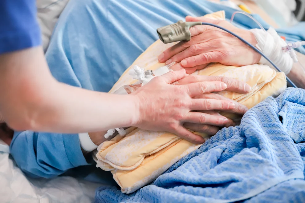 En medarbetare inom vården har lagt sin ena hand på en patients hand.